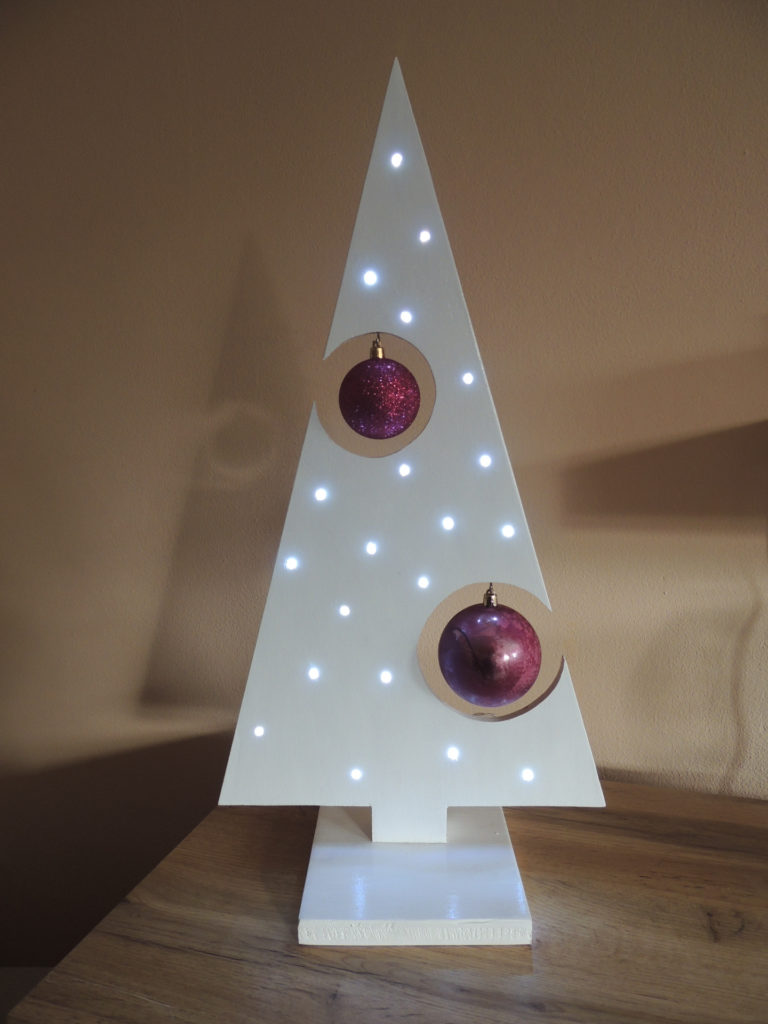 Holzbaum in weiß mit zwei Magentafarbenen Kugeln. Beleuchtet mit einer Lichterkette in kaltem Weiß.